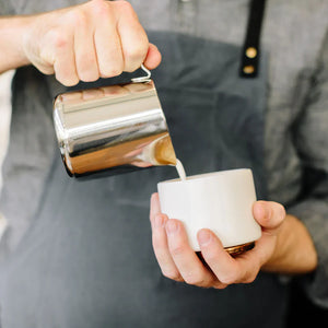 Barista nalewa mleko z polerowanego dzbanka ze stali nierdzewnej, część akcesoriów do Espresso i dzbanek do mleka, wszystko o kawie.
