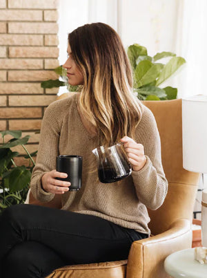 Kobieta w beżowym swetrze z baristycznym dzbankiem do espresso ze szkła, nowoczesny design, Najnowsze wiadomości, wszystko o kawie.