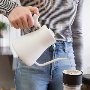 Ręka nalewająca wodę z białego czajnika z wąskim dzióbkiem do filtra do kawy, część EspressoGear, wszystko o kawie.